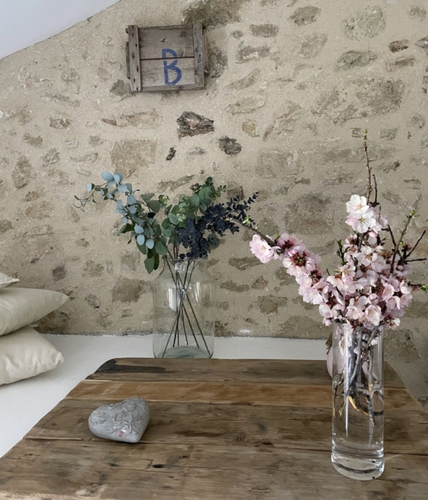 A vase with pink flowers and holly branches decorating a wooden table near a stone wall.