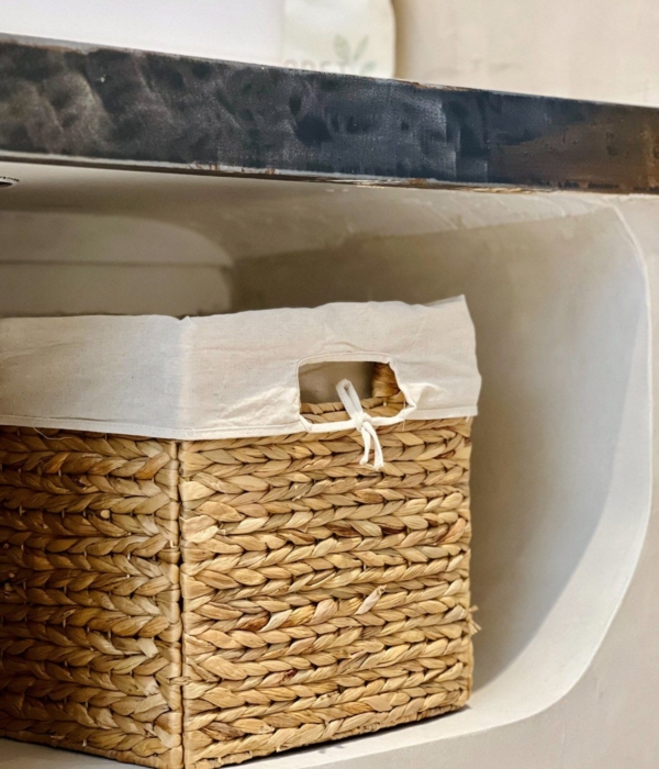 A natural wicker basket with a white canvas lid, placed on a shelf.