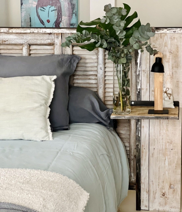 A cozy bedroom with a whitewashed wooden bed, grey cushions and a houseplant.