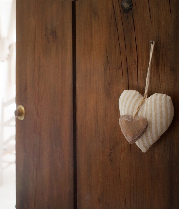 A felt heart hanging from a dark wooden door, leading into a bright and warm room.