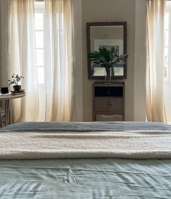 A peaceful room with a comfortable bed, a mirror and linen curtains.