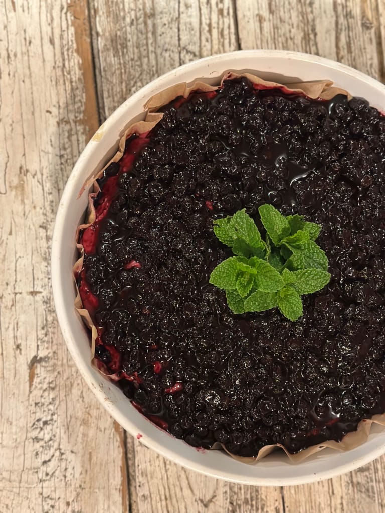A delicious dessert of fresh red berries in a white ramekin on a wooden base.