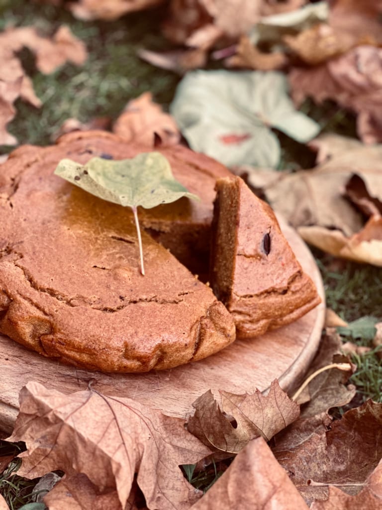 Un gâteau d'automne décoré avec une feuille, sur une planche en bois, entouré de feuilles mortes.