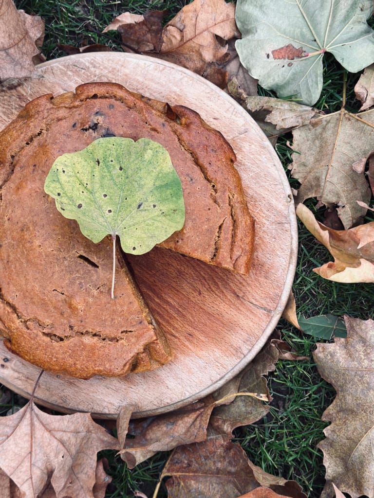 Gâteau d'automne décoré d'une feuille verte sur une assiette en bois, entouré de feuilles mortes.