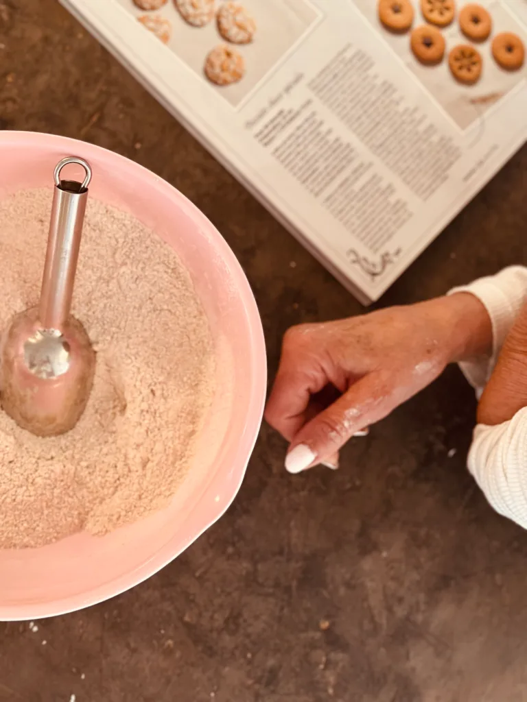 A hand prepares a cookie recipe in a bowl with a spatula.