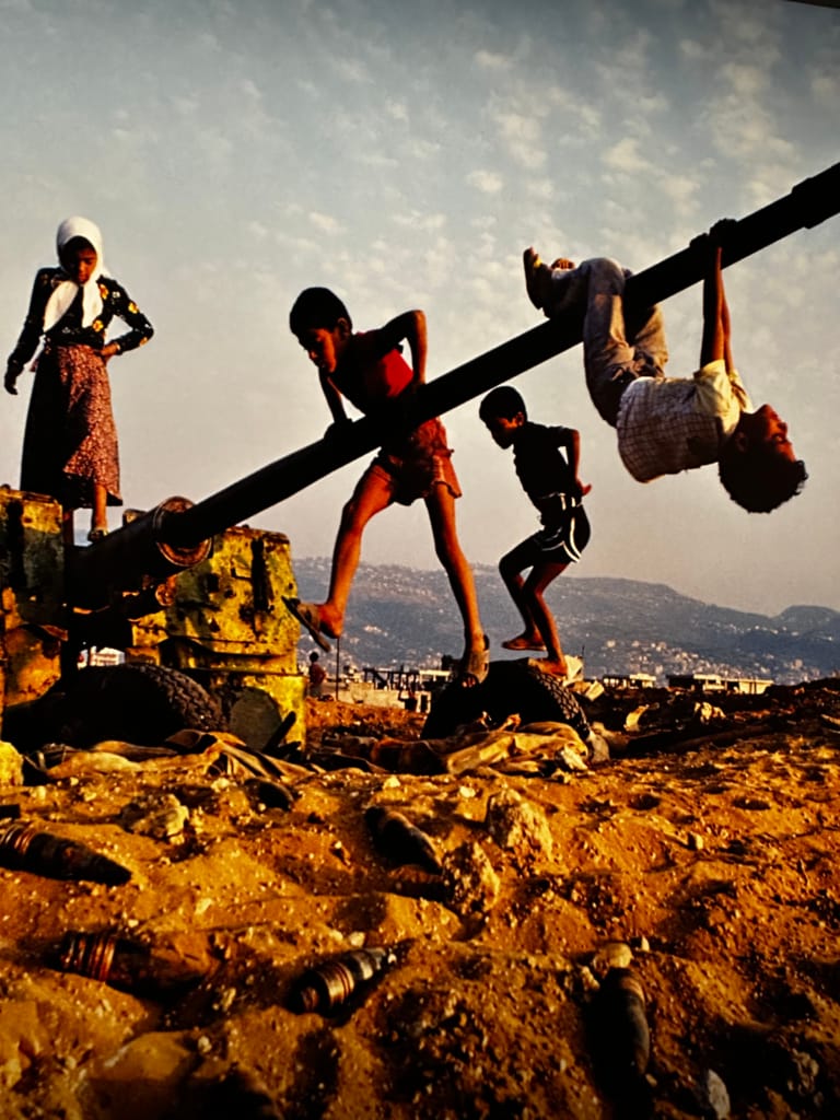 Children playing on an abandoned tank in a desolate landscape at sunset.