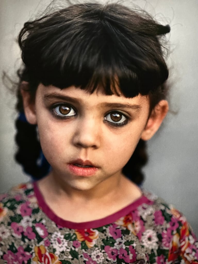 Enfilé une robe fleurie, une jeune fille regarde fixement la caméra avec des yeux expressifs.