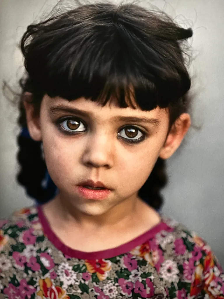 Ein junges Mädchen in einem geblümten Kleid blickt mit ausdrucksvollen Augen konzentriert in die Kamera.