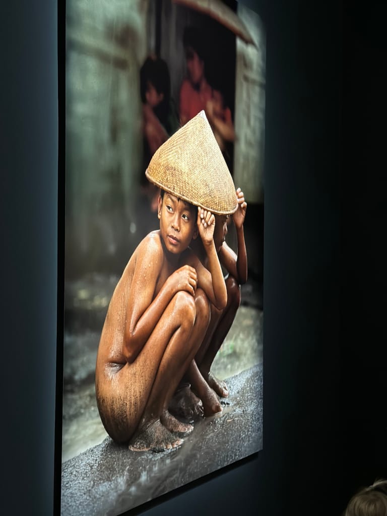 A young, barefoot boy wears a loincloth hat in a rainy Vietnamese village.