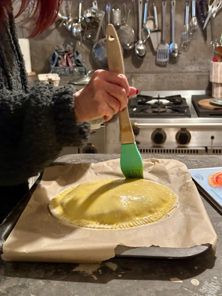A person applies grease to a pie crust in a kitchen.