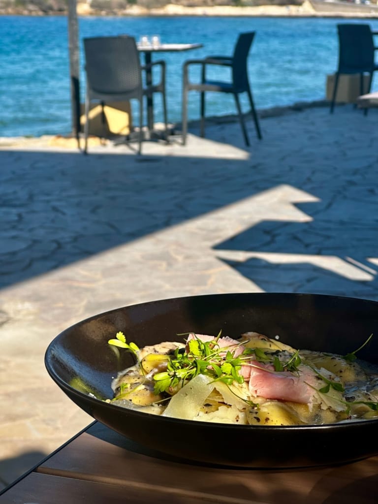 A delicious pasta dish with prosciutto and fresh herbs, served by the sea.