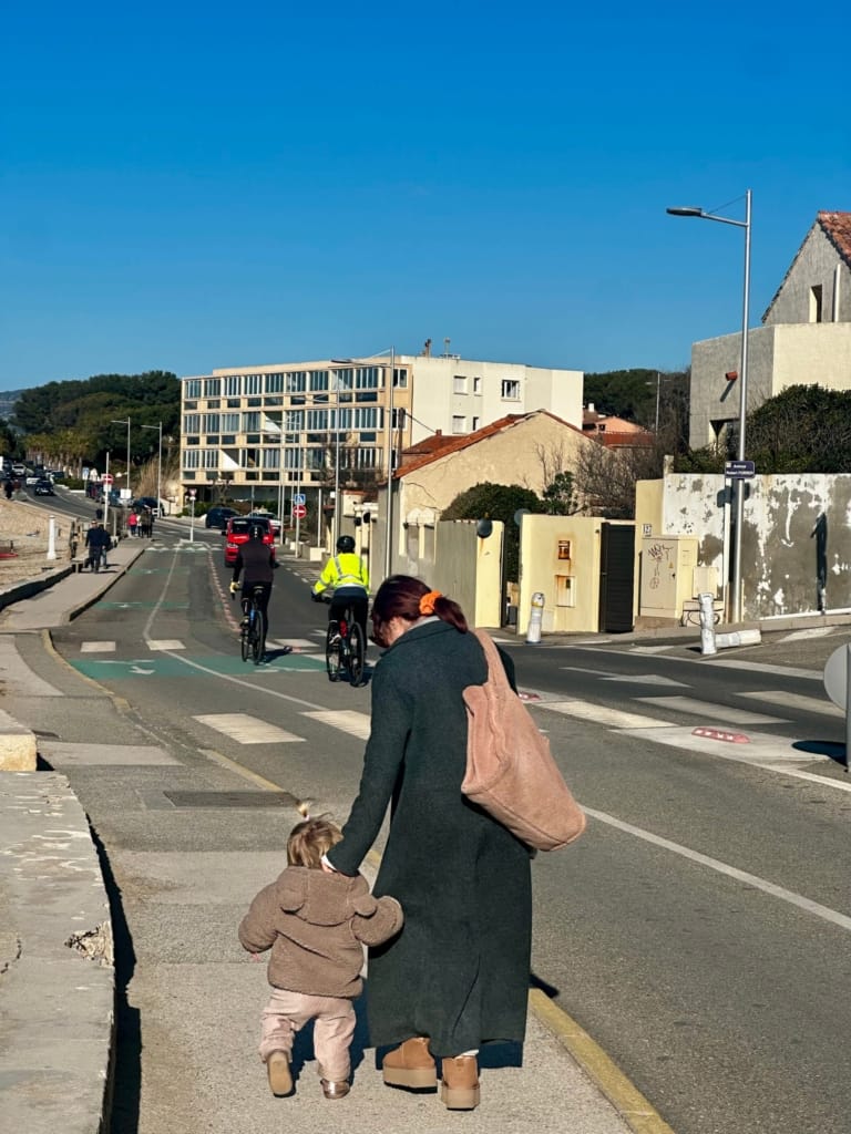 A woman walks with her child on a cycle path during the day, in front of a modern building.