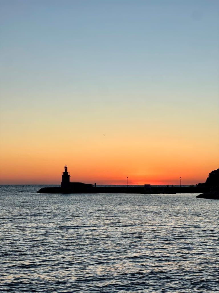 Silhouette d'un phare sur l'océan au coucher du soleil, une scène paisible et colorée.