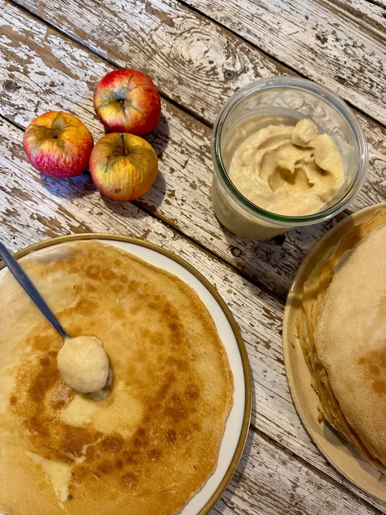 Pfannkuchen mit Apfelmus und ein paar frischen Äpfeln auf einem Holztisch.