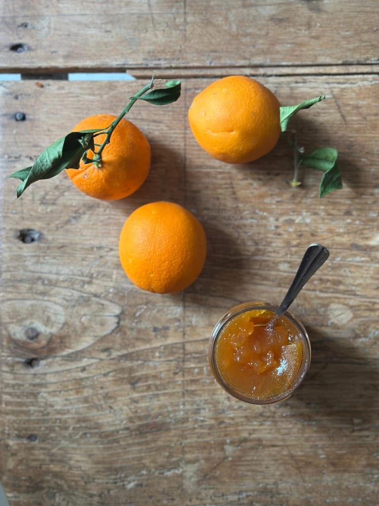 Fresh oranges and citrus jam on an old wooden board.