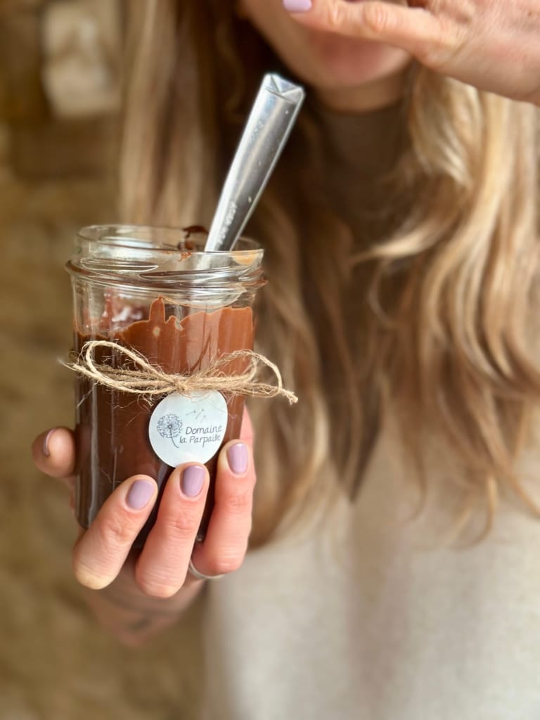 A hand holds a jar of spread, ready to be eaten with a spoon.
