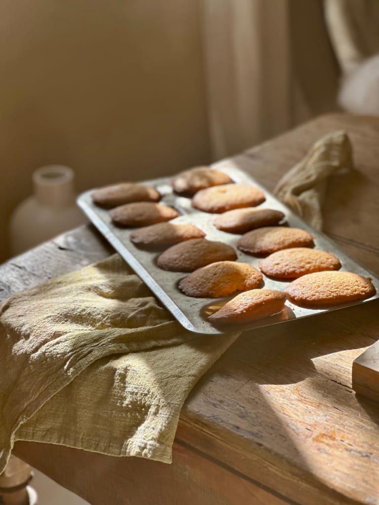Ein Backblech voller köstlicher, goldgelber Madeleines auf einem beleuchteten Holztisch.