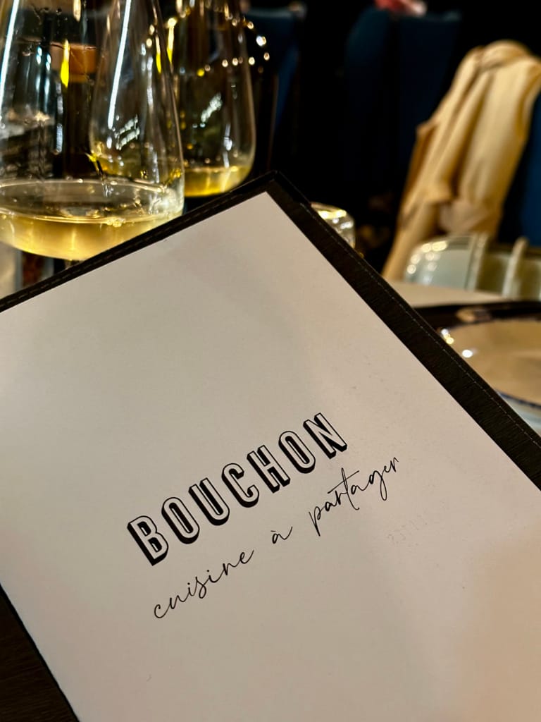 Menu from the Bouchon restaurant, sharing dishes, with a glass of wine.