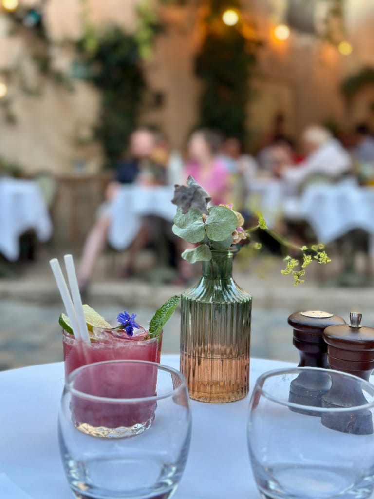 Ein hübsch gedeckter Tisch auf der Terrasse mit Cocktails und Blumen, eine freundliche Atmosphäre.
