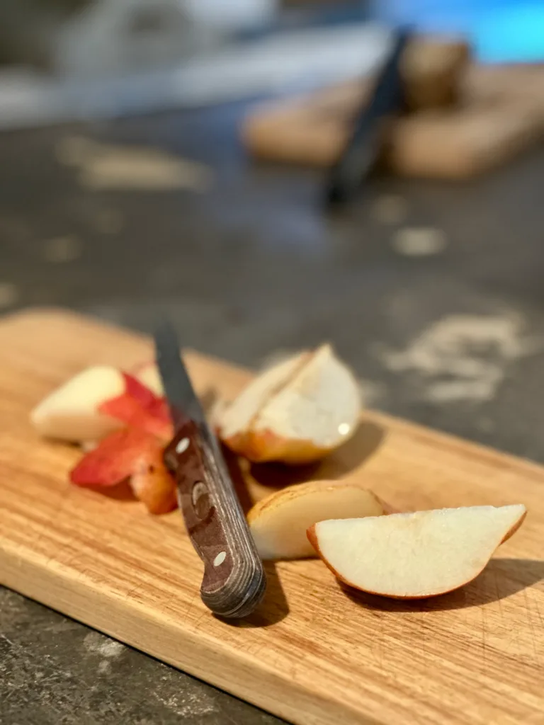 Des tranches de poire et un couteau sur une planche à découper en bois.