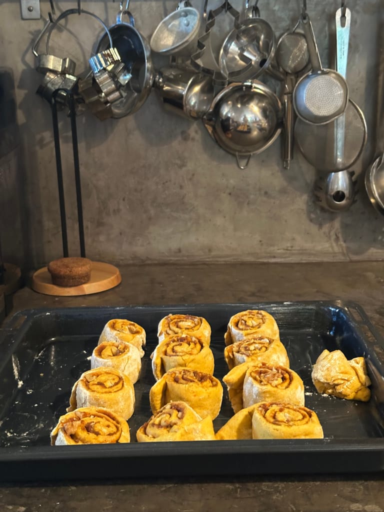 Rolls of crepe stuffed with cinnamon are arranged on a baking sheet in a kitchen.