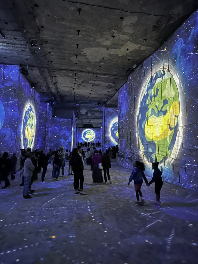 Des gens admirent des projections lumineuses d'une planète sur les murs d'un tunnel.
