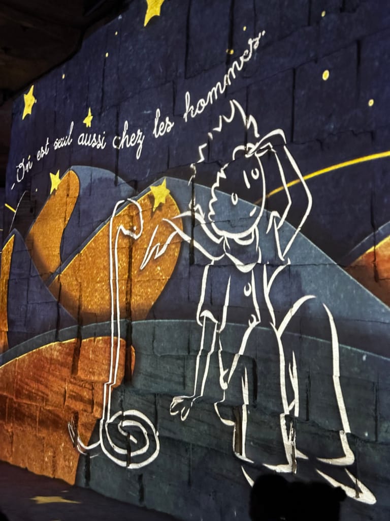 Mur décoratif avec le Petit Prince et son proverbe, ambiance lumineuse et poétique.