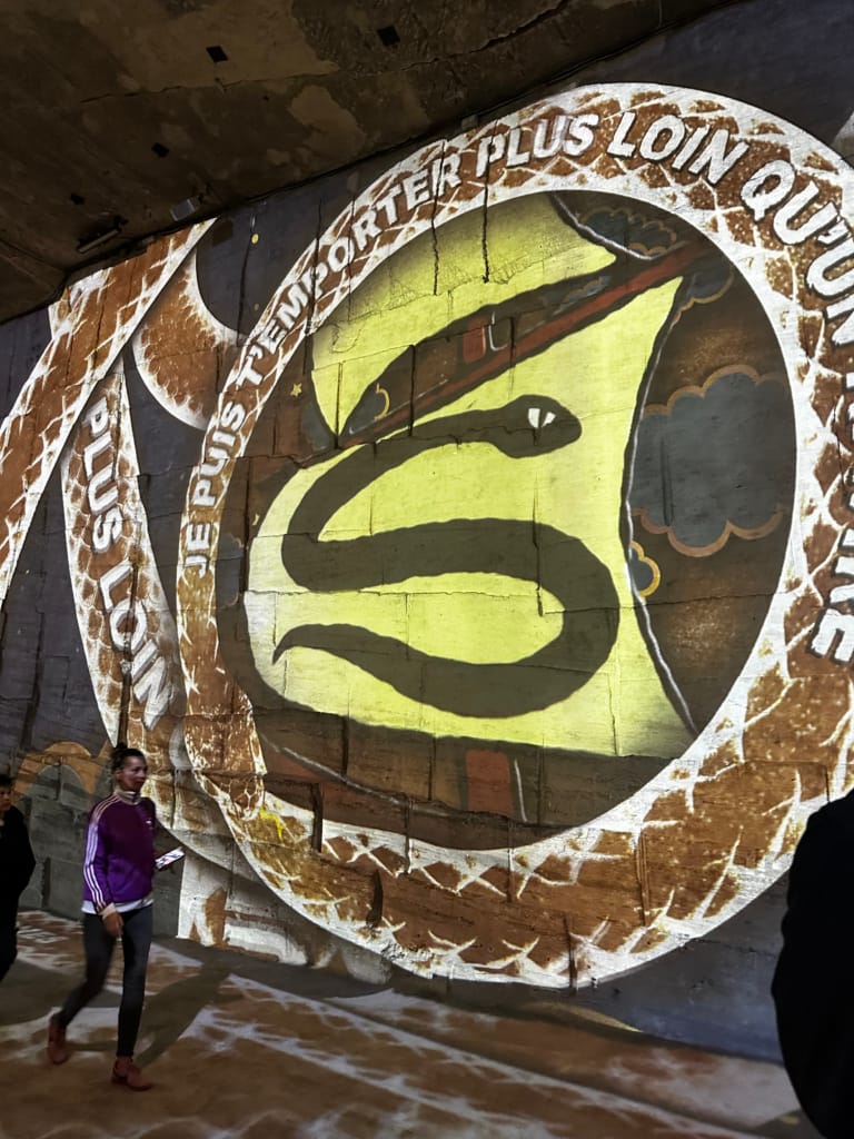 Fresque lumineuse d'un serpent dans un tunnel, message "Je puis t'emporter plus loin qu'un éclair".