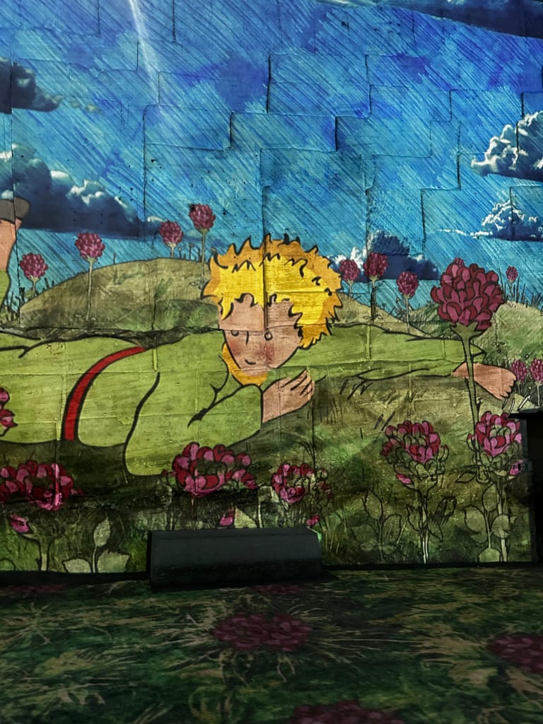 Un mur décoré représentant le Petit Prince, dans un paysage champêtre coloré et rêveur.