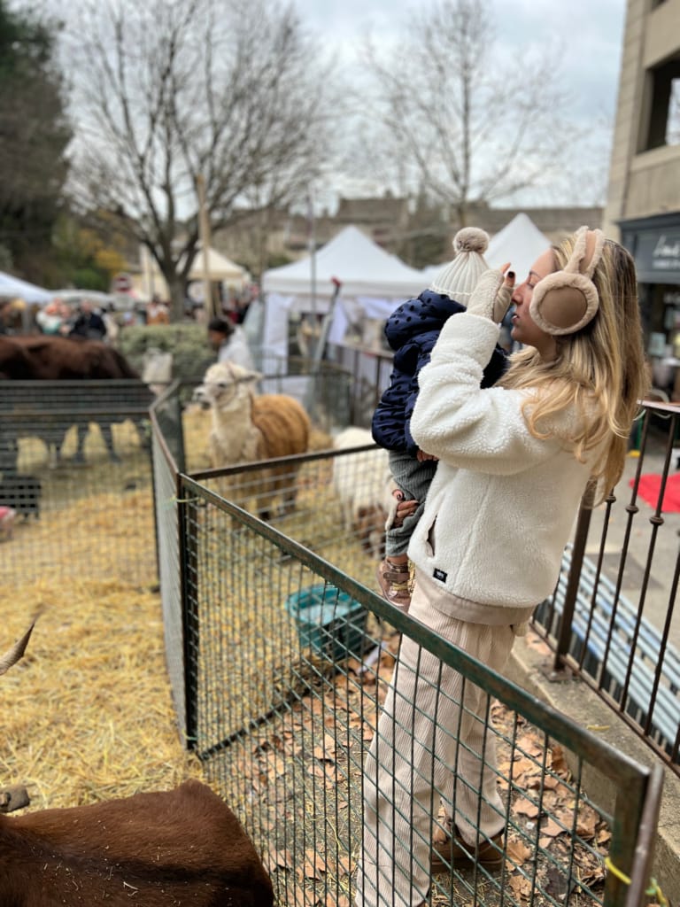 Une femme observe un troupeau de moutons avec son bébé au marché de Noël.