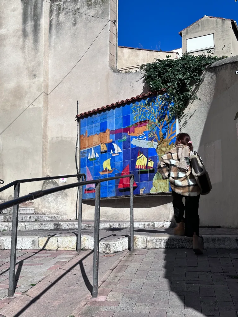 Mosaïque colorée représentant des bateaux et des scènes maritimes sur un mur extérieur.