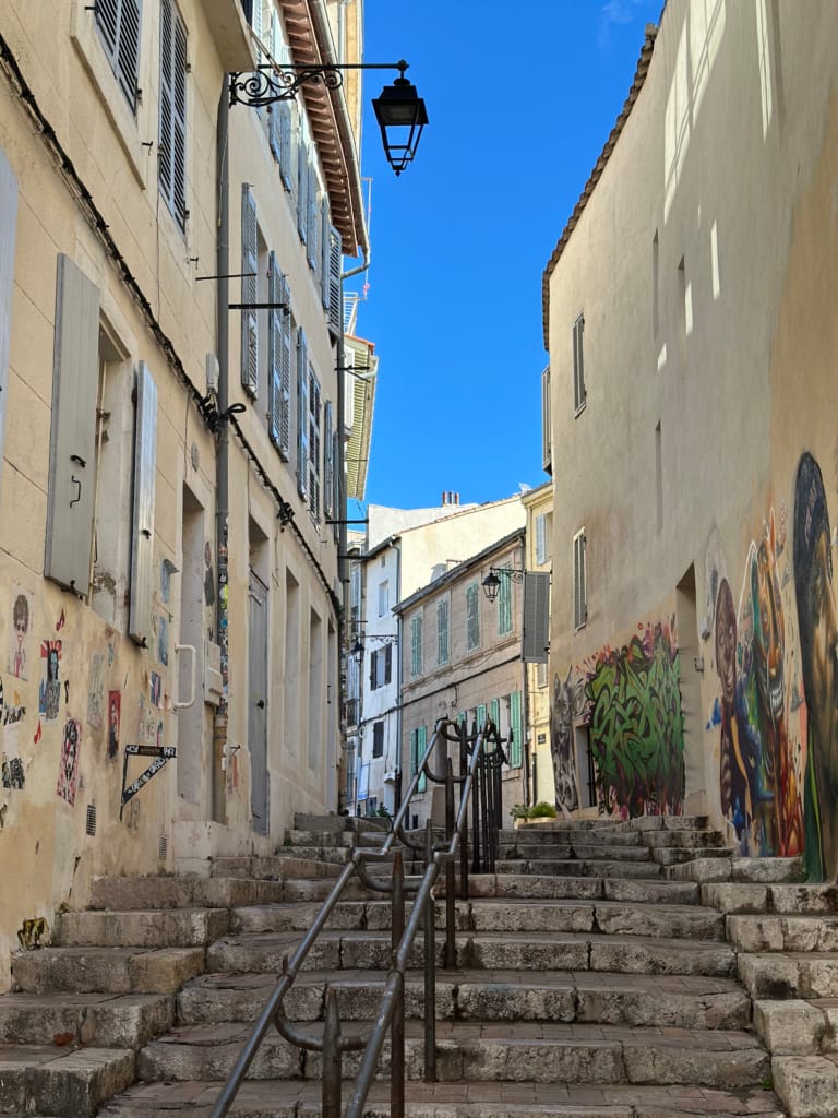 Une ruelle pavée pittoresque avec des bâtiments colorés et des escaliers menant vers le haut sous un ciel bleu.