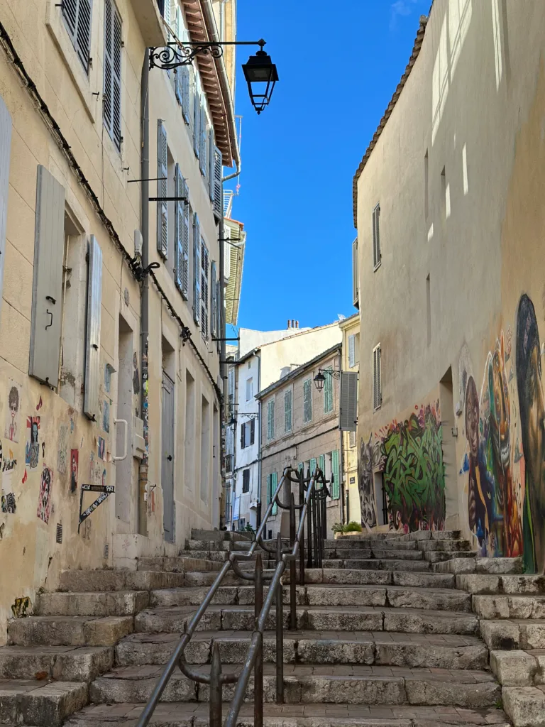 A picturesque cobbled alley with colorful buildings and stairs leading upwards under a blue sky.
