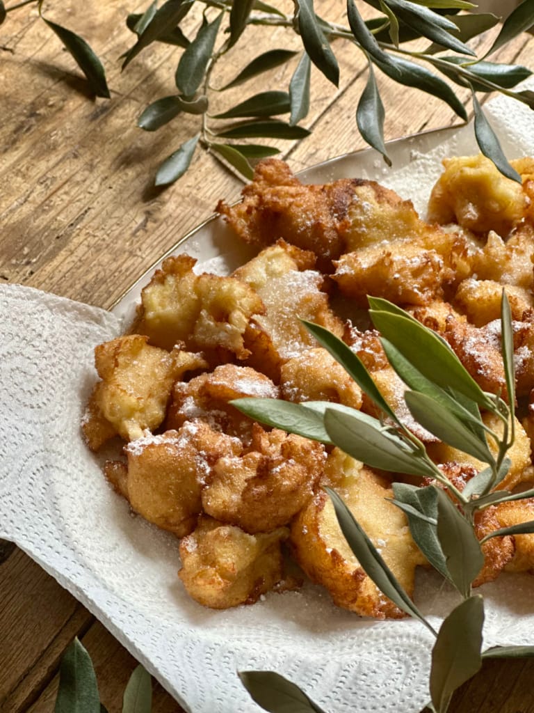 Des beignets frits et sucrés, garnis de sucre glace, accompagnés d'olives fraîches.