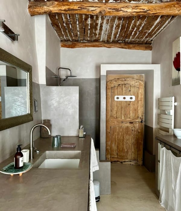 Salle de bain rustique avec un sol en béton, un meuble vasque et un ancien placard en bois.