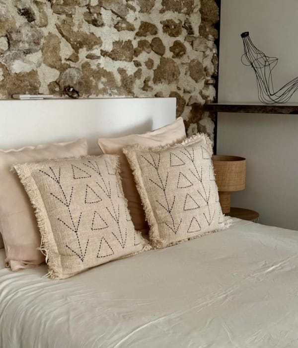 Coussins décoratifs en lin beige avec motifs géométriques sur un lit en chambre rustique.