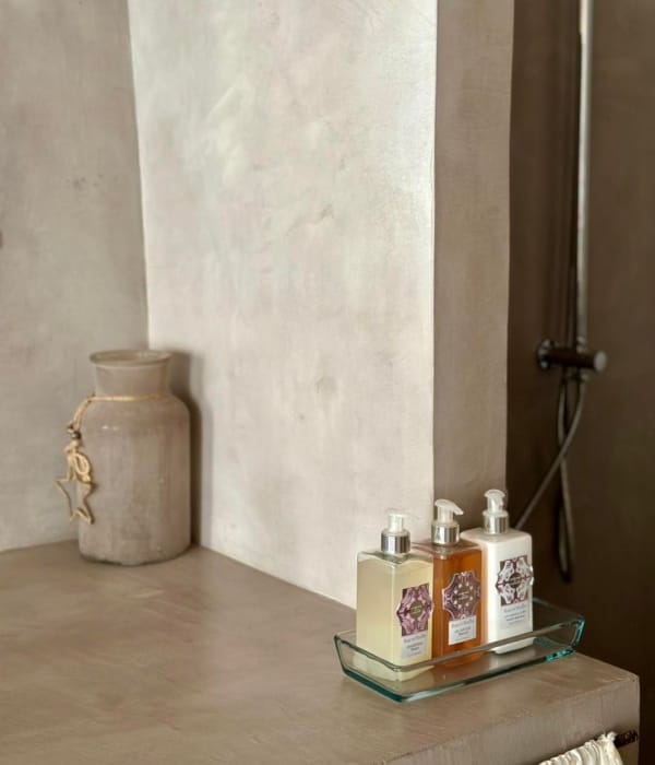 Sur une table, des flacons de savon et un pot en céramique se trouvent dans un décor neutre.