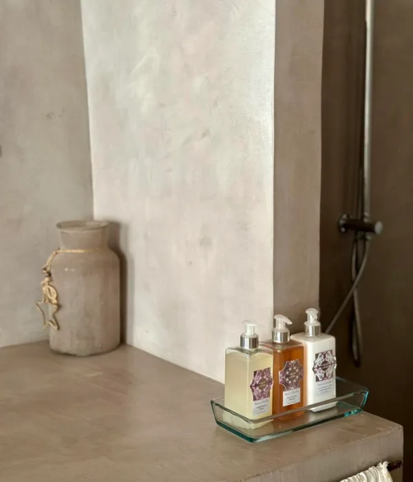 Sur une table, des flacons de savon et un pot en céramique se trouvent dans un décor neutre.