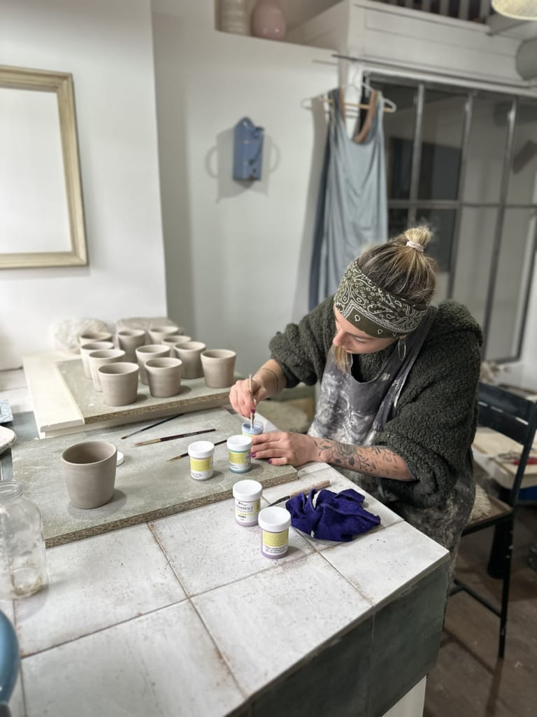 Une artiste peint des poteries dans son atelier, concentrée sur ses créations.