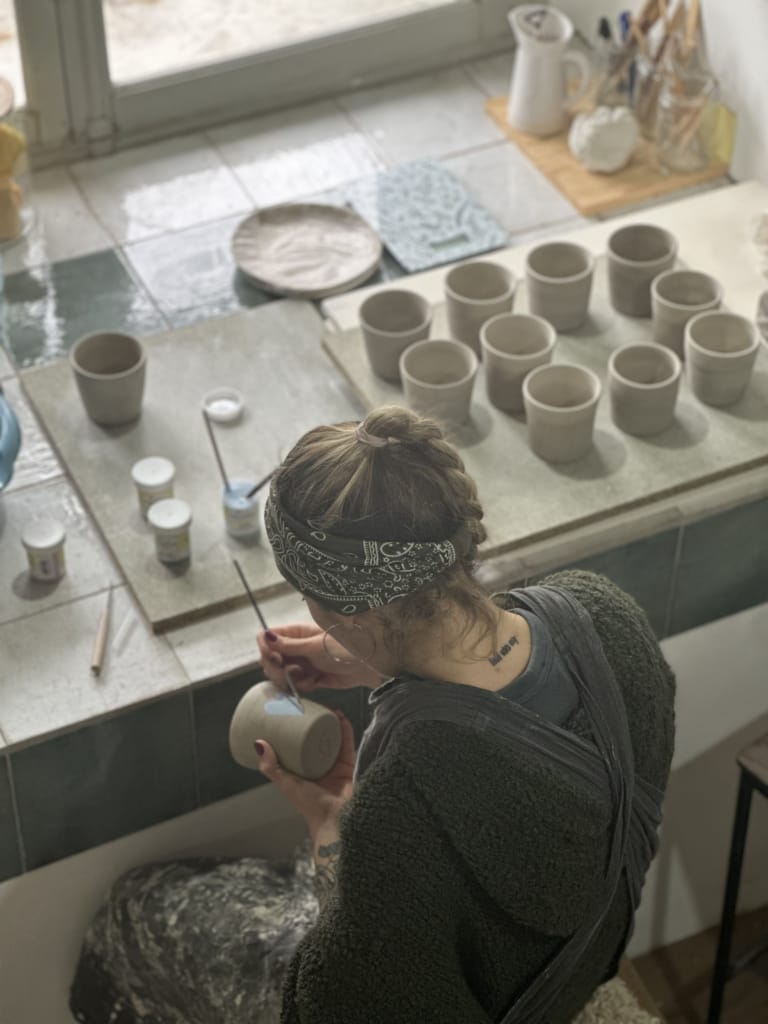 Une céramiste travaille sur des pots dans son atelier, concentrée sur sa création.