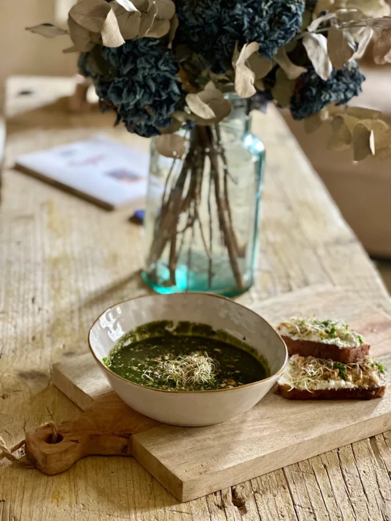 Une soupe verte crémeuse et une tartine garnie de micro-algues sur une planche en bois rustique.