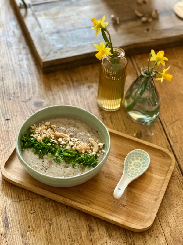 Une soupe crémeuse aux noix et persil frais, servie sur une planche en bois avec des narcisses.
