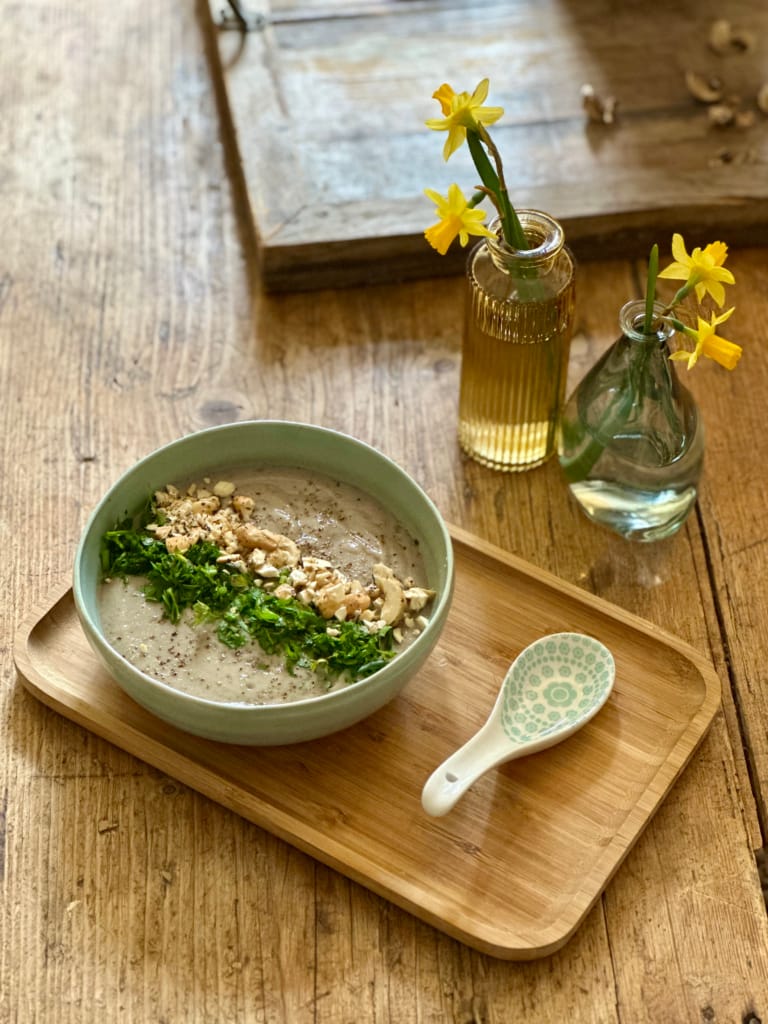 Eine cremige Suppe mit Walnüssen und Petersilie, serviert in einer Schüssel auf einem Bambustablett.