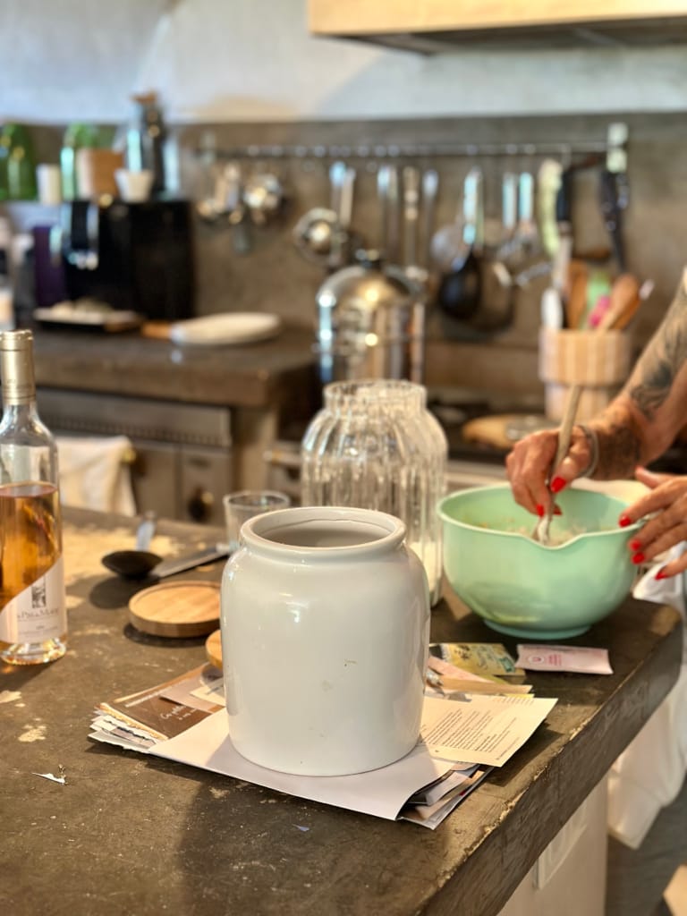 Une femme prépare une recette dans une cuisine, avec un grand pot blanc en évidence.
