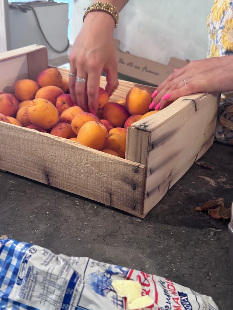 Une personne trie des abricots mûrs dans une caisse en bois rustique.