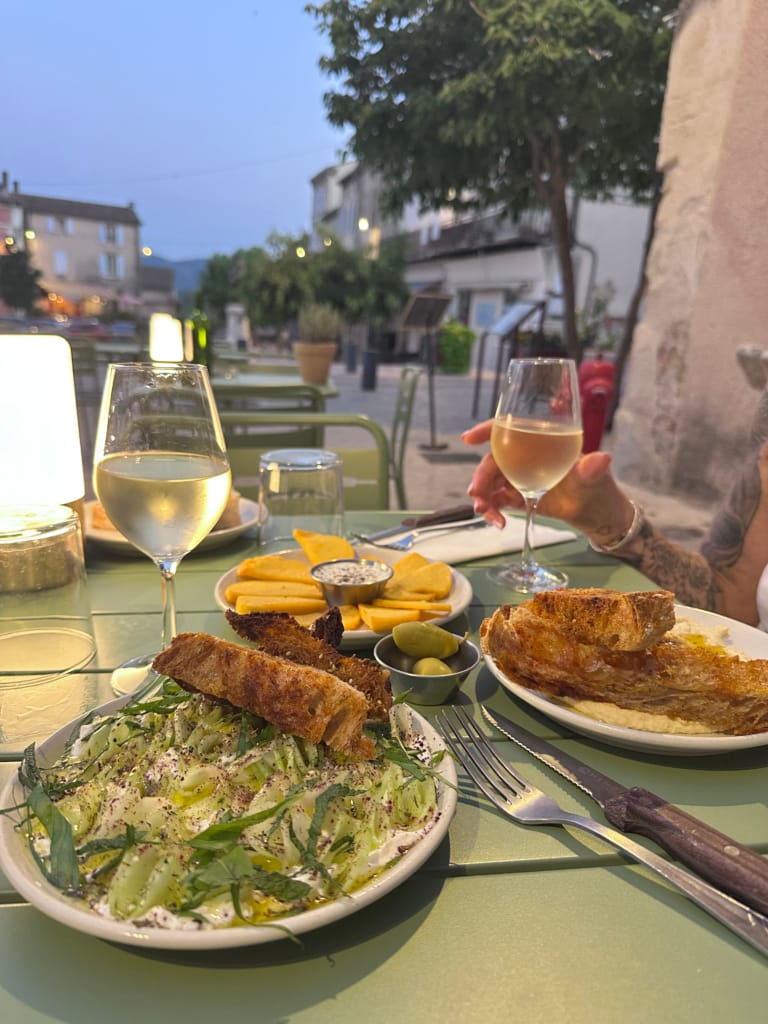 Ein Terrassentisch mit einer Auswahl an Vorspeisen, Toast und zwei Gläsern Weißwein in der Abenddämmerung.