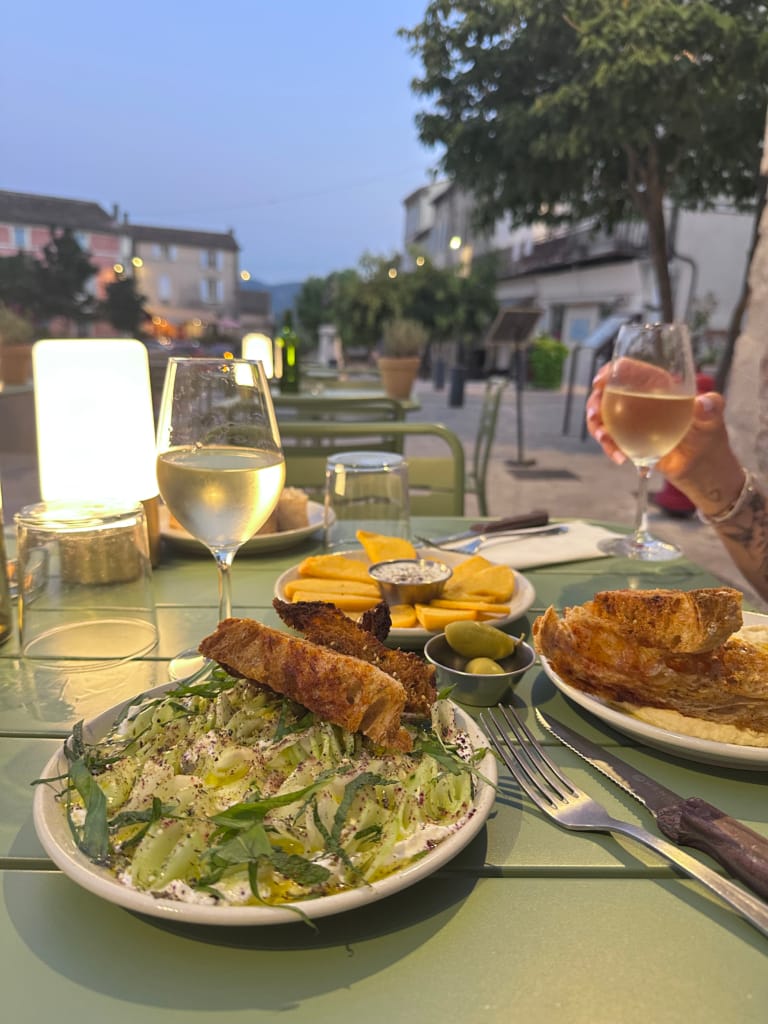 Ein Terrassentisch mit Mezze, Toast und zwei Gläsern Weißwein in der Abenddämmerung.