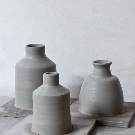 Trois vases en terre cuite crue, posés sur une planche, prêts à être cuits.