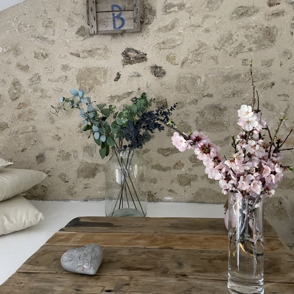 A vase with pink flowers and holly branches decorating a wooden table near a stone wall.