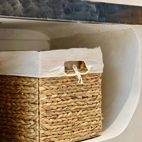 A natural wicker basket with a white canvas lid, placed on a shelf.